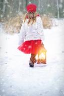 Girl in white and red clothing, with the lantern, among the beautiful, white snow in winter