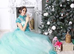 a girl in a princess dress sits by a Christmas tree