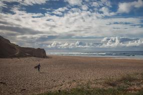 Beautiful landscape of the sandy beach, among the mountains, with the surfer girl, under the blue sky with white clouds