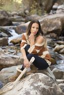 young woman sits on rock at stream