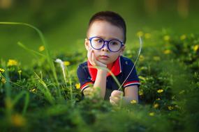 little boy with glasses in green grass in blurred background