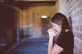 girl prays against a brick wall