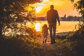 father with little daughter outside among the plants at colorful sunset background