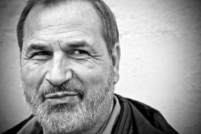 Black and white photo, with the portrait of the smiling, man, with the beard, near the wall