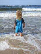 a child in a swimming suit on the beach looks at the waves