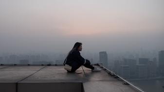 a lonely girl sits on the roof of a building at dusk