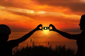 the word hope is held in the hands of mom and daughter on a background of golden sunset