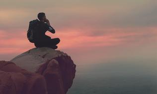 young man with backpack sits on rock at scenic sky