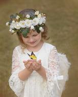 Smiling girl child in white flower crown and dress, holding beautiful and colorful butterfly