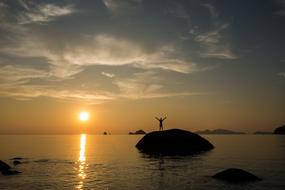 man with raised hands on a stone in the ocean in Thailand, kho lipe