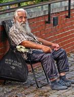 elderly homeless man is sitting on a chair