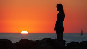 lonely girl on the seashore against the background of a bright orange sunset