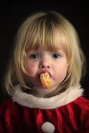 photo of a little girl with a slice of tangerine in her mouth