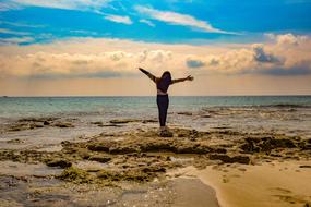 young Girl stands with wide open hands on Beach