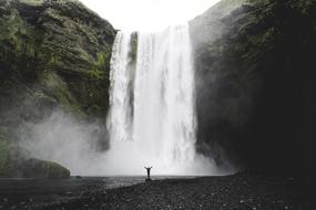 person stands with wide open hands in front of gorgeous Waterfall, Iceland