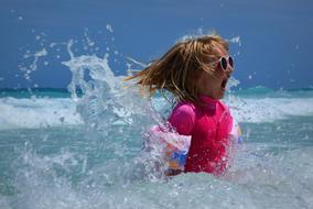 girl in a pink bathing suit is splashing in the sea