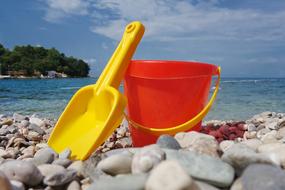 Yellow scoop and red and yellow bucket toys, on the rocky beach