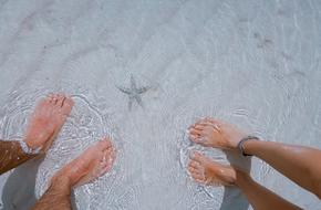 Feet of the guy and girl, in the beautiful, clear sea, with the cute starfish