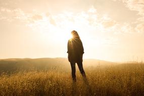 young girl in casual clothing stands on meadow in back light
