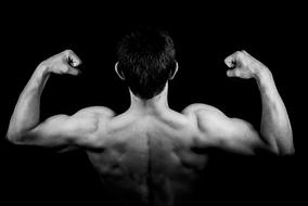 Black and white back view of a man showing muscles at black background