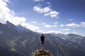 Man, standing on the beautiful cliff, among the mountains, at blue sky with white clouds on background