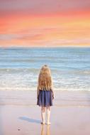 long haired caucasian child girl stands on wet Sand in front of sea