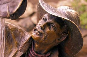 Shiny, bronze sculpture of the Wishful Thinkin Cowboy, in the park of Colorado, in light