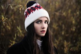 Portrait of the beautiful, young girl in ornamental, white, red and black hat in autumn