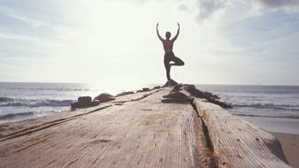 girl meditates on a wooden pier by the ocean