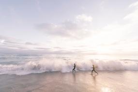 two persons running on Beach to foamy wave