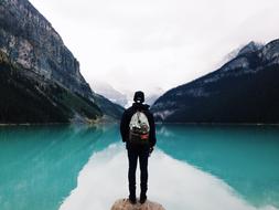 man with backpack near mountain lake with turquoise water