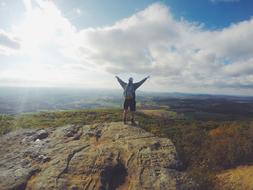 man with wide open hands standing on rock at scenic landscape