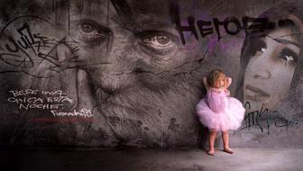 Child girl in pink dress posing at dark wall with Graffiti