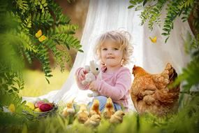 little girl sitting on green grass next to a chicken