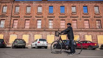 old man with bicycle stands on road at old brick building