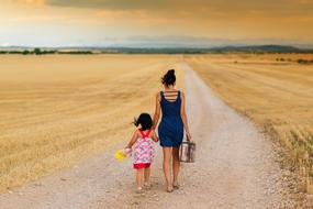 mom and daughter are walking along a rural road