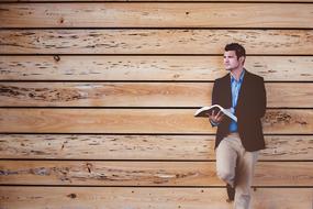 man reading a book near a wooden wall