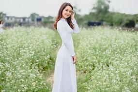 Nice girl in long dress posing on blooming meadow