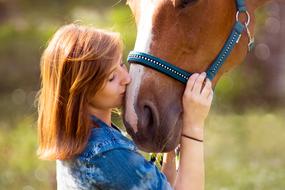Girl kissing cute brown and white horse on green blurred background