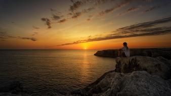 a girl sitting on a rock during sunset