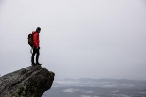 Guy with backpack, standing on the cliff, above the beautiful, foggy waterscape