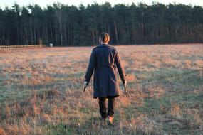a man in a raincoat walks on arable field