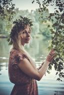 girl in a wreath under a tree near the water
