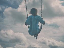 photo of a girl on a swing against the background of clouds