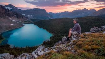 Sitting man, looking on the beautiful, turquoise lake, among the green trees on the mountains