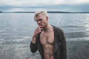 photo of blond with fingers on his face against the background of the sea