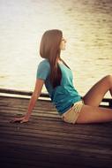 Pretty Young Girl rests on wooden pier at water