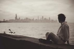 Man Sitting on Seaside in view of city