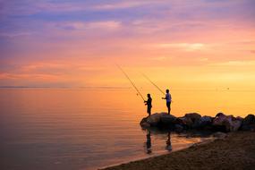 People, fishing on the beautiful coast, at colorful, gradient sunset on horizon of Aegean Sea in Greece