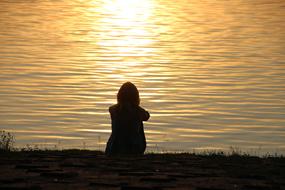 back view of girl silhouette sitting on Lakeside at sunset